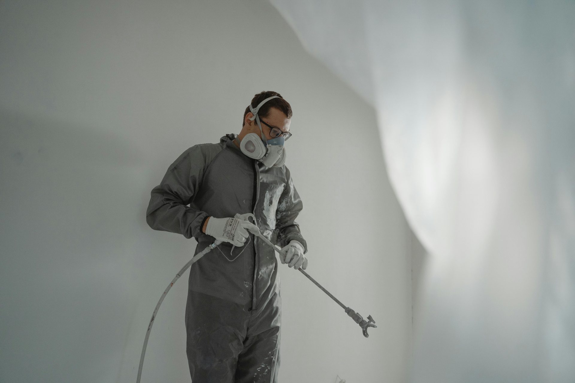Eine Person in Schutzkleidung streicht eine Wand und veranschaulicht damit Hausrenovierungsarbeiten.